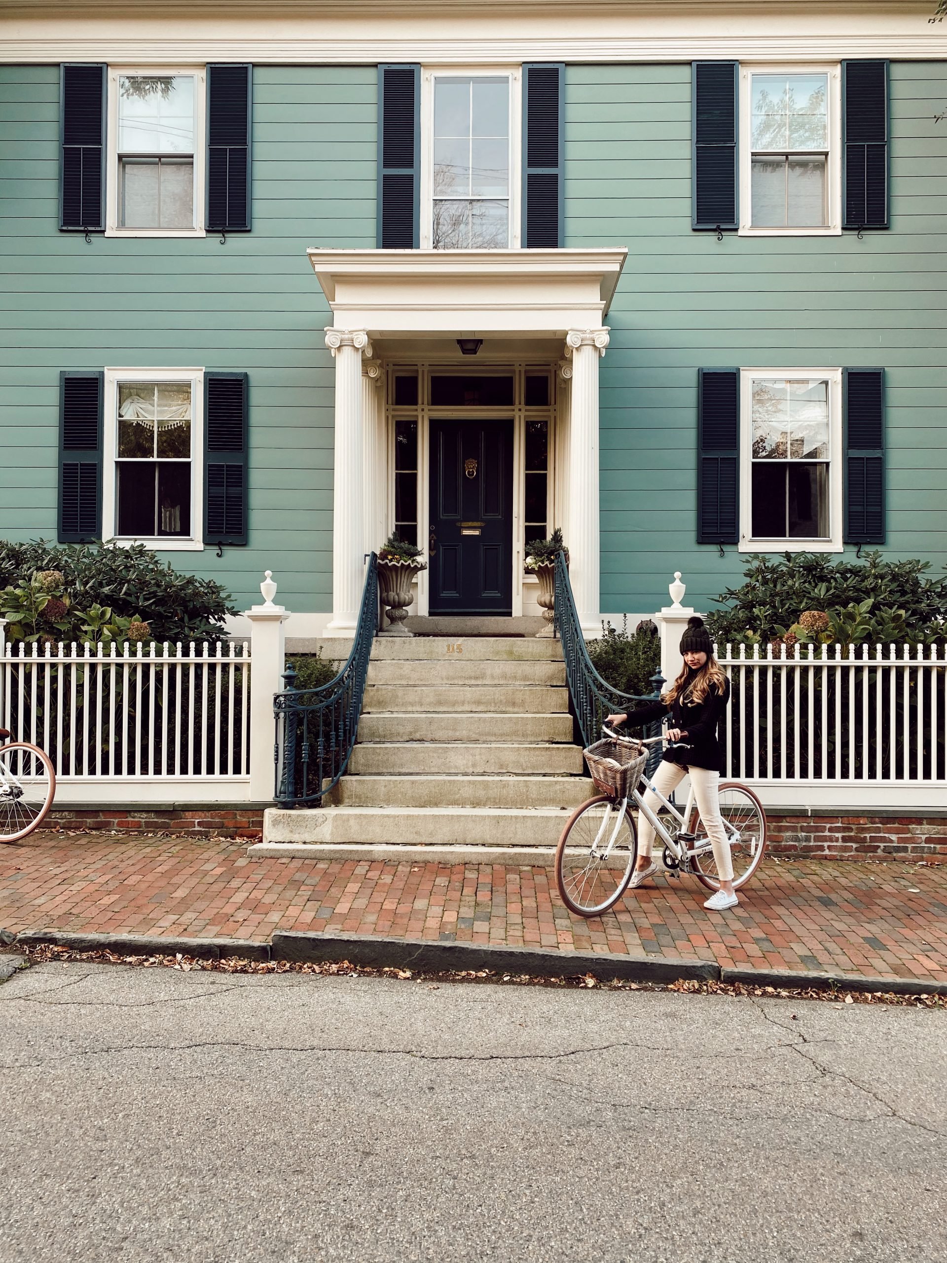a large sea green historic home with a woman on a bicycle in front of it